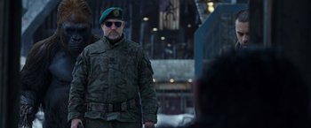 Movie still from “War for the Planet of the Apes” (2017), directed by Matt Reeves – A man in a military uniform is standing in front of a building; Medium shot, Over the shoulder angle