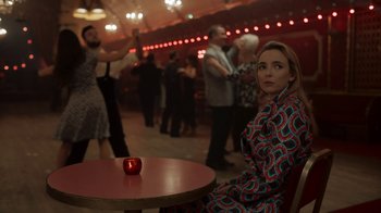 Movie still from “Killing Eve” (2018), created by Phoebe Waller-Bridge – A woman sitting at a table in front of an apple; Medium shot, Over the shoulder angle