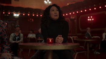 Movie still from “Killing Eve” (2018), created by Phoebe Waller-Bridge – A woman sitting at a table with a candle in front of her; Medium shot, Over the shoulder angle