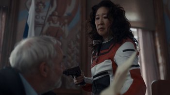 Movie still from “Killing Eve” (2018), created by Phoebe Waller-Bridge – A woman holding a gun while standing next to a man; Medium shot, Over the shoulder angle