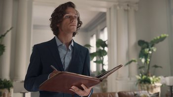 Movie still from “Killing Eve” (2018), created by Phoebe Waller-Bridge – A man in a suit holding an open book; Medium shot, Low angle