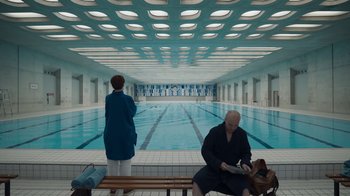 Movie still from “Killing Eve” (2018), created by Phoebe Waller-Bridge – A man and a woman sitting in front of an indoor swimming pool; Wide shot, Over the shoulder angle