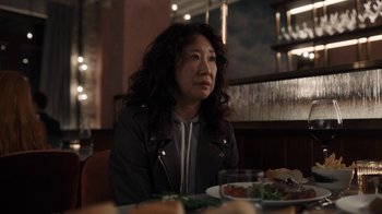 Movie still from “Killing Eve” (2018), created by Phoebe Waller-Bridge – A woman sitting at a table in front of a plate of food; Medium shot, Over the shoulder angle
