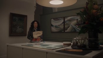 Movie still from “Killing Eve” (2018), created by Phoebe Waller-Bridge – A woman standing in front of a counter holding a paper bag; Wide shot, High angle