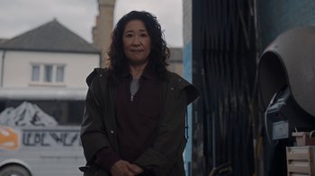 Movie still from “Killing Eve” (2018), created by Phoebe Waller-Bridge – A woman standing in front of a gate; Medium shot, Over the shoulder angle