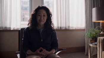 Movie still from “Killing Eve” (2018), created by Phoebe Waller-Bridge – A woman sitting in a chair in front of a window; Medium shot, Over the shoulder angle