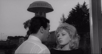 Movie still from “L'Eclisse” (1962), directed by Michelangelo Antonioni – A man and a woman standing next to each other in front of a building; Medium shot, Low angle