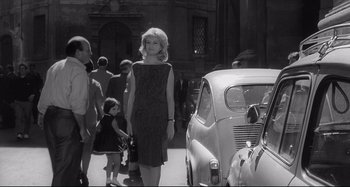 Movie still from “L'Eclisse” (1962), directed by Michelangelo Antonioni – A black and white photo of a woman and a car; Wide shot, Low angle