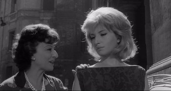 Movie still from “L'Eclisse” (1962), directed by Michelangelo Antonioni – Two women standing next to each other on a city street; Close Up shot, Low angle