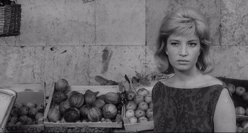 Movie still from “L'Eclisse” (1962), directed by Michelangelo Antonioni – A black and white photo of a woman in front of boxes of fruit; Close Up shot, Low angle