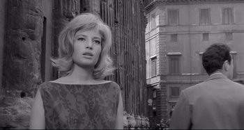 Movie still from “L'Eclisse” (1962), directed by Michelangelo Antonioni – A black - and - white photo of a woman in front of a building; Close Up shot, Low angle