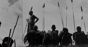 Movie still from “L'Eclisse” (1962), directed by Michelangelo Antonioni – A group of people sitting in a field with spears; Wide shot, Low angle