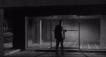 Movie still from “L'Eclisse” (1962), directed by Michelangelo Antonioni – A black and white photo of a man standing in front of a window; Wide shot, Low angle