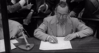 Movie still from “L'Eclisse” (1962), directed by Michelangelo Antonioni – An old photo of a man writing on a piece of paper; Medium shot, High angle