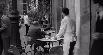 Movie still from “L'Eclisse” (1962), directed by Michelangelo Antonioni – Two men sitting at a table outside a restaurant; Wide shot, Over the shoulder angle