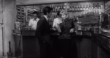 Movie still from “L'Eclisse” (1962), directed by Michelangelo Antonioni – A man and a woman standing at a bar talking; Medium shot, Over the shoulder angle