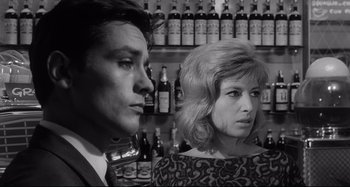 Movie still from “L'Eclisse” (1962), directed by Michelangelo Antonioni – A man and a woman standing next to each other in front of bottles; Close Up shot, Low angle