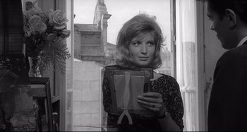Movie still from “L'Eclisse” (1962), directed by Michelangelo Antonioni – A black and white photo of a woman holding a suitcase; Medium shot, Over the shoulder angle
