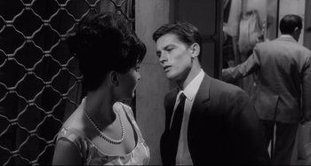 Movie still from “L'Eclisse” (1962), directed by Michelangelo Antonioni – A man and a woman standing next to each other in front of a building; Medium shot, Over the shoulder angle