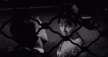 Movie still from “L'Eclisse” (1962), directed by Michelangelo Antonioni – A man and a woman looking at each other through a fence; Close Up shot, Over the shoulder angle