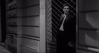Movie still from “L'Eclisse” (1962), directed by Michelangelo Antonioni – A man standing in front of a metal fence; Medium shot, Low angle