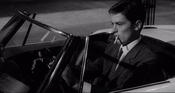 Movie still from “L'Eclisse” (1962), directed by Michelangelo Antonioni – A black and white photo of a man smoking a cigarette; Medium shot, High angle