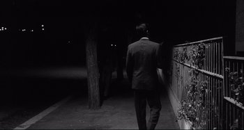 Movie still from “L'Eclisse” (1962), directed by Michelangelo Antonioni – A black and white photo of a man in a suit walking down the street; Medium shot, Over the shoulder angle