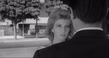 Movie still from “L'Eclisse” (1962), directed by Michelangelo Antonioni – A man and a woman standing next to each other in front of a building; Close Up shot, Over the shoulder angle