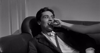 Movie still from “L'Eclisse” (1962), directed by Michelangelo Antonioni – A man sitting on a couch eating a piece of food; Close Up shot, High angle