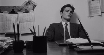 Movie still from “L'Eclisse” (1962), directed by Michelangelo Antonioni – A black and white photo of a man sitting at a desk; Medium shot, High angle