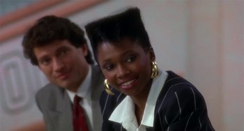 Movie still from “L.A. Story” (1991), directed by Mick Jackson – A woman with a very large mohawk haircut smiles for the camera; Close Up shot, Over the shoulder angle