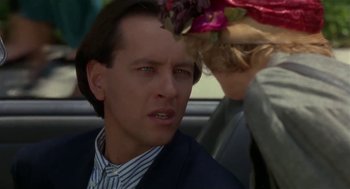Movie still from “L.A. Story” (1991), directed by Mick Jackson – A person in a car wearing a suit; Close Up shot, Over the shoulder angle