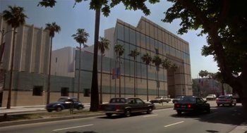Movie still from “L.A. Story” (1991), directed by Mick Jackson – Cars driving down a street past a large building with palm trees; Extreme Wide shot, Low angle