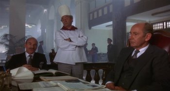 Movie still from “L.A. Story” (1991), directed by Mick Jackson – A man wearing a chef's hat standing in front of a table; Medium shot, Over the shoulder angle