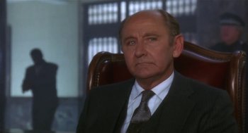 Movie still from “L.A. Story” (1991), directed by Mick Jackson – An older man wearing a suit and tie sitting in an office chair; Close Up shot, Low angle