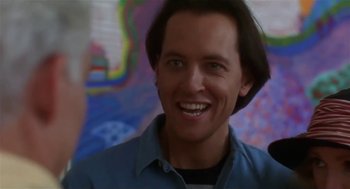 Movie still from “L.A. Story” (1991), directed by Mick Jackson – A man with long brown hair smiling for the camera; Close Up shot, Over the shoulder angle