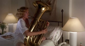 Movie still from “L.A. Story” (1991), directed by Mick Jackson – A woman sitting on a bed playing a tuba; Medium shot, Low angle