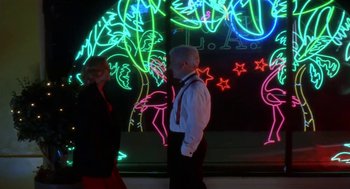 Movie still from “L.A. Story” (1991), directed by Mick Jackson – A man and a woman are standing in front of a wall of neon lights; Wide shot, Low angle