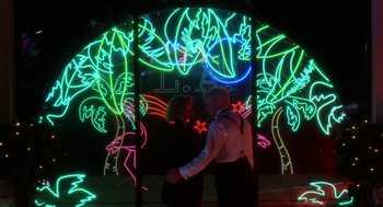 Movie still from “L.A. Story” (1991), directed by Mick Jackson – A man standing in front of a neon sign at night; Wide shot, Low angle