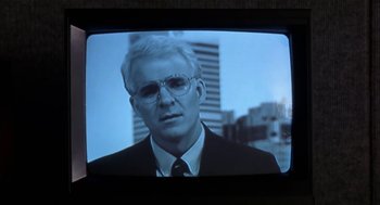Movie still from “L.A. Story” (1991), directed by Mick Jackson – A man wearing a suit and tie on a television screen; Close Up shot, Over the shoulder angle
