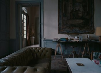 Movie still from “La Belle Noiseuse” (1991), directed by Jacques Rivette – A living room filled with furniture next to an open door; Wide shot, High angle