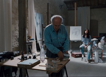 Movie still from “La Belle Noiseuse” (1991), directed by Jacques Rivette – An older man is working on a painting in a studio; Wide shot, Low angle