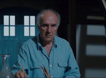 Movie still from “La Belle Noiseuse” (1991), directed by Jacques Rivette – An older man is holding a pair of pencils; Medium shot, Low angle