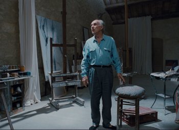 Movie still from “La Belle Noiseuse” (1991), directed by Jacques Rivette – An older man standing in a room with paintings on the walls; Wide shot, Low angle