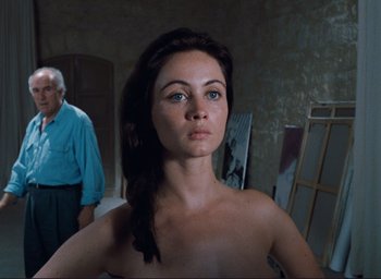 Movie still from “La Belle Noiseuse” (1991), directed by Jacques Rivette – A young woman standing next to an older man in an art studio; Medium shot, Over the shoulder angle