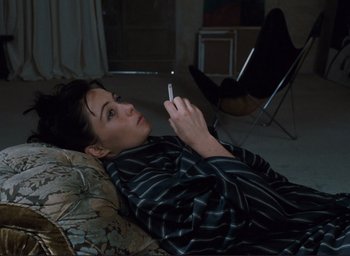 Movie still from “La Belle Noiseuse” (1991), directed by Jacques Rivette – A man laying on the ground while holding a cigarette; Medium shot, High angle