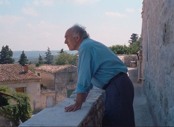 Movie still from “La Belle Noiseuse” (1991), directed by Jacques Rivette – An older man leaning on a wall looking over the top of a building; Medium shot, Low angle