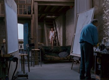 Movie still from “La Belle Noiseuse” (1991), directed by Jacques Rivette – A woman sitting on top of a couch in a room; Wide shot, Low angle
