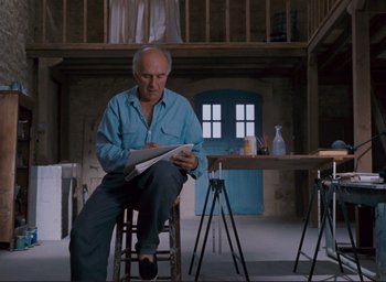 Movie still from “La Belle Noiseuse” (1991), directed by Jacques Rivette – An older man sitting at a table reading a newspaper; Wide shot, Low angle