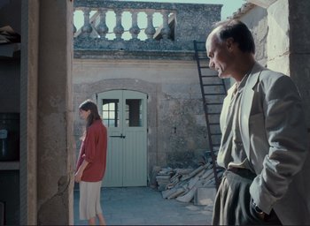 Movie still from “La Belle Noiseuse” (1991), directed by Jacques Rivette – A man and a woman standing in front of a building; Wide shot, Low angle